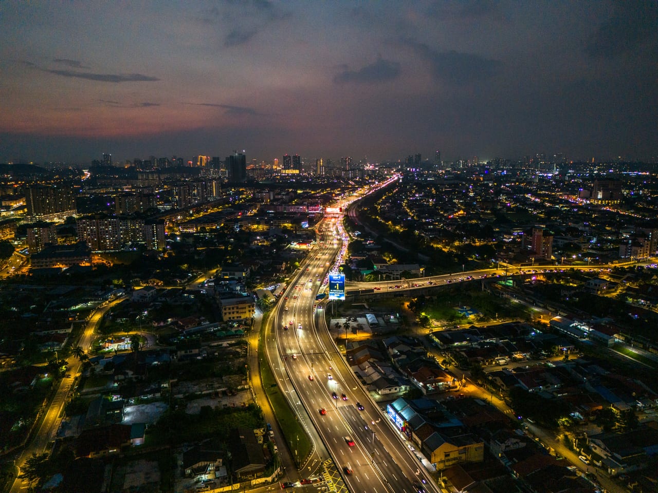 Old Klang Road sunset aerial — highway interchange and the KL skyline